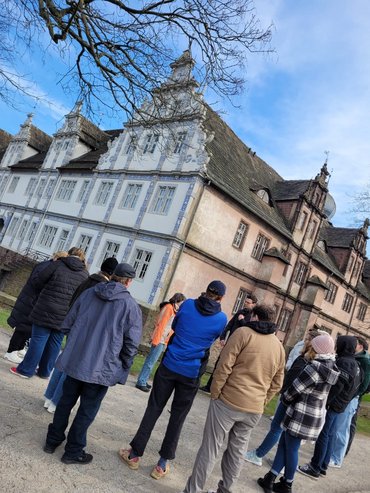 Menschen vor einem historischen Gebäude. Die Perspektive des Fotos ist nach recht gekippt
