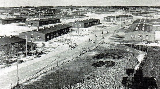 Historisches schwarz-weiß Foto. Luftaufnahme. In der Mitte ein Weg, links und rechts einstöckige Baracken.