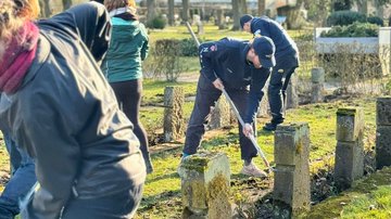 Mehrere Personen die die Flächen vor langen Reihen von Grabkreuzen reinigen.