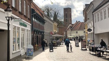 Eine Fußgängerzone mit Pflastersteinen. Alte Gebäude mit kleinen Geschäften. Einige Menschen sind hier unterwegs.