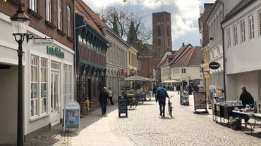 Eine Fußgängerzone mit Pflastersteinen. Alte Gebäude mit kleinen Geschäften. Einige Menschen sind hier unterwegs.