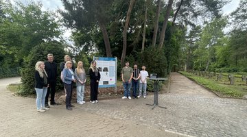 Schülergruppe rechts und links von der Informationstafel. Außerdem Schulleiter und Bürgermeisterin links neben der Tafel stehend. 
